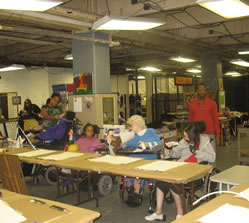 Three participating arts work at long tables in the Independence Art Studio.