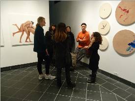 A circle of five people stand in discussion in an art gallery.