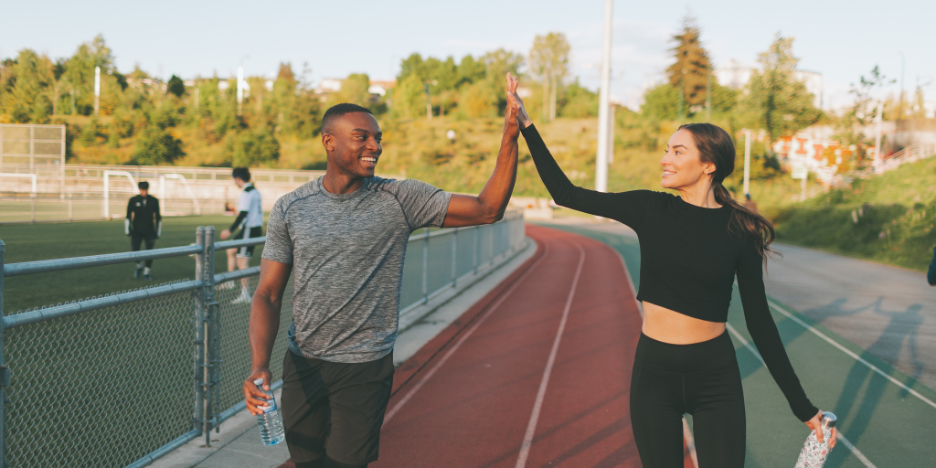Man and woman walking on a track, giving each other a high five.